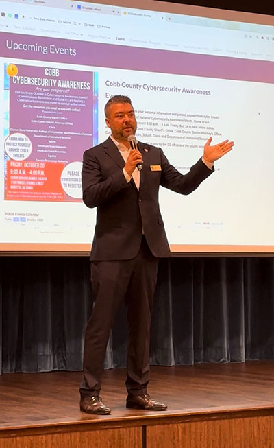 Kevin standing on a stage with a projector in the background while speaking about cybersecurity