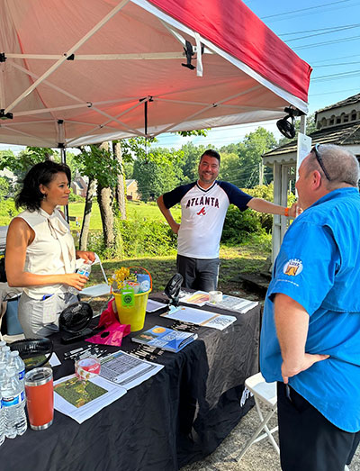 Kevin and commissioner Jerica Richardson standing beneath a tent at an event speaking to a male constituent