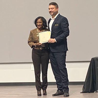 Kevin smiling standing next to woman jointly holding up a certificate