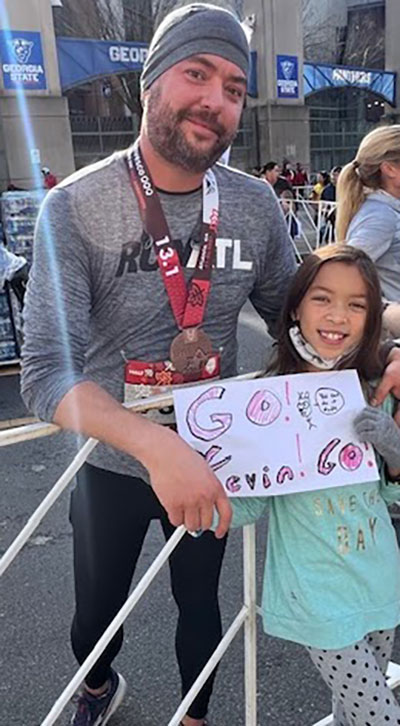 Kevin standing next to daughter wearing a medal after a running event