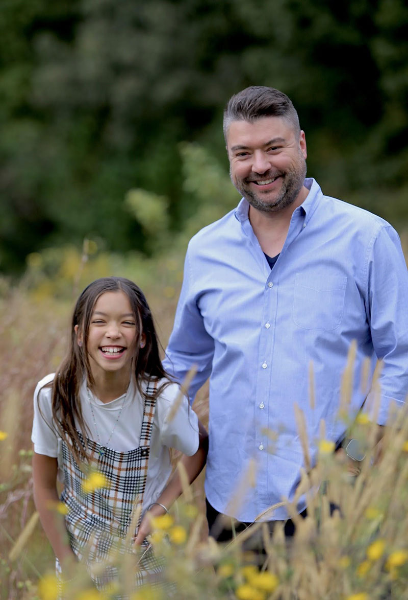 Kevin standing in a field of flowers next to young daughter