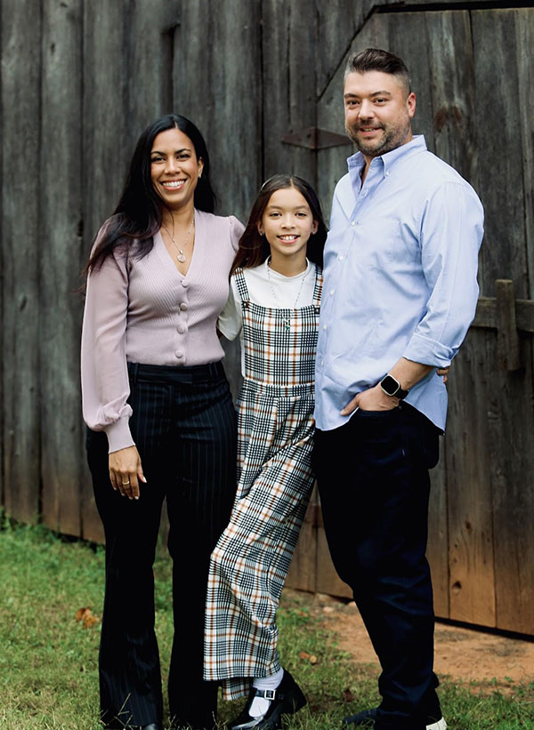 Kevin standing with young daughter and wife in front of a fence