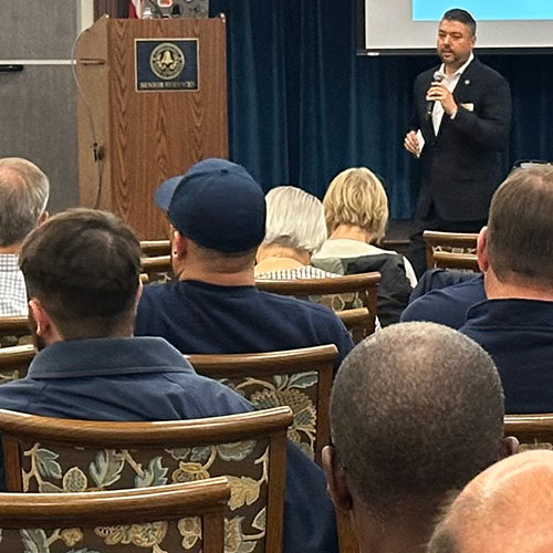 Kevin standing at a forum in front of seated rows of community members