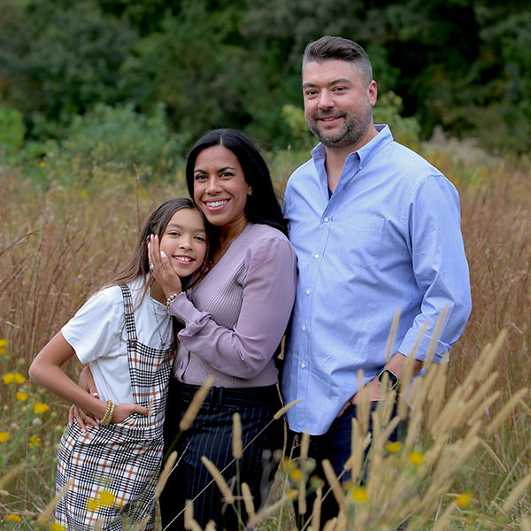 Kevin with wife and daughter smiling in a field